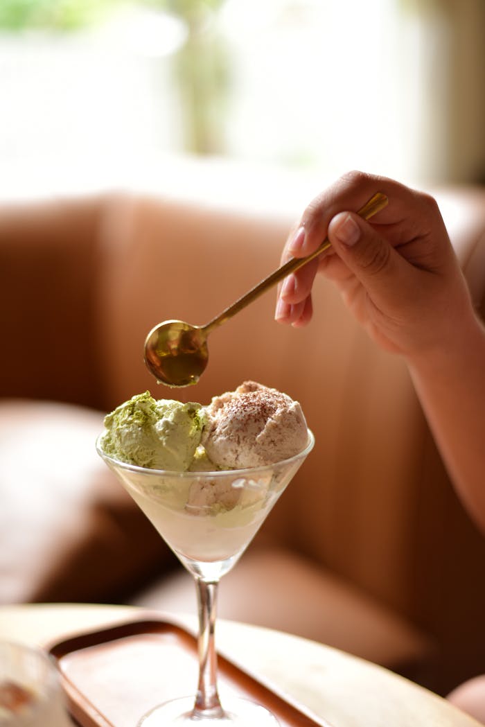 services-01 Hand holding spoon over ice cream in elegant glass bowl, indoor setting.