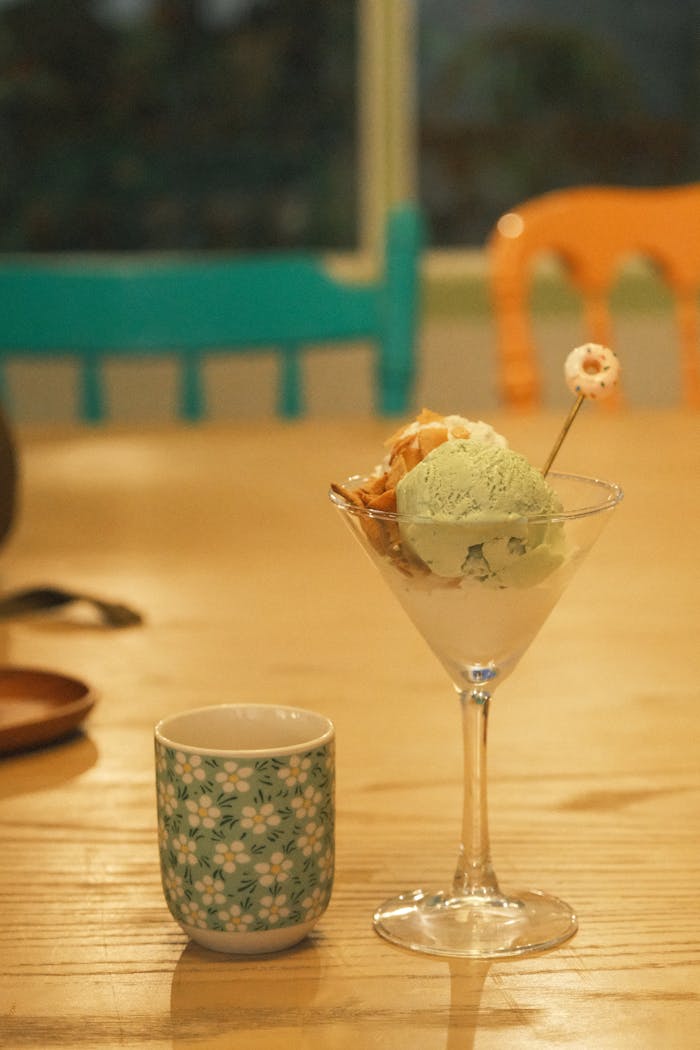 A vibrant dessert with green tea ice cream and a tea cup on a wooden table.